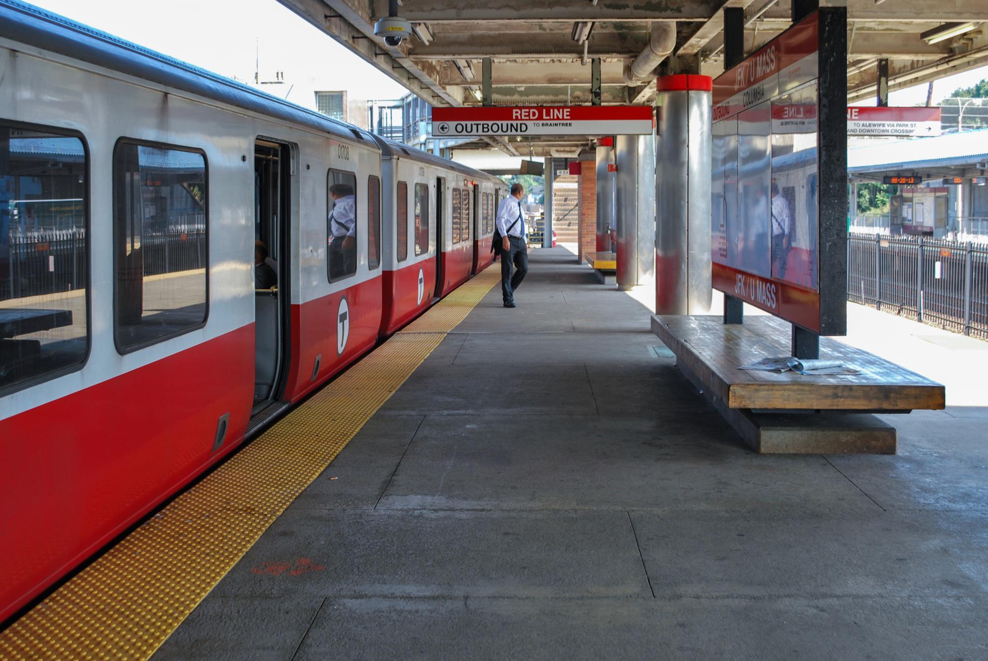 A man on the sunlit JFK/UMass platform, with a Red Line train pulled up