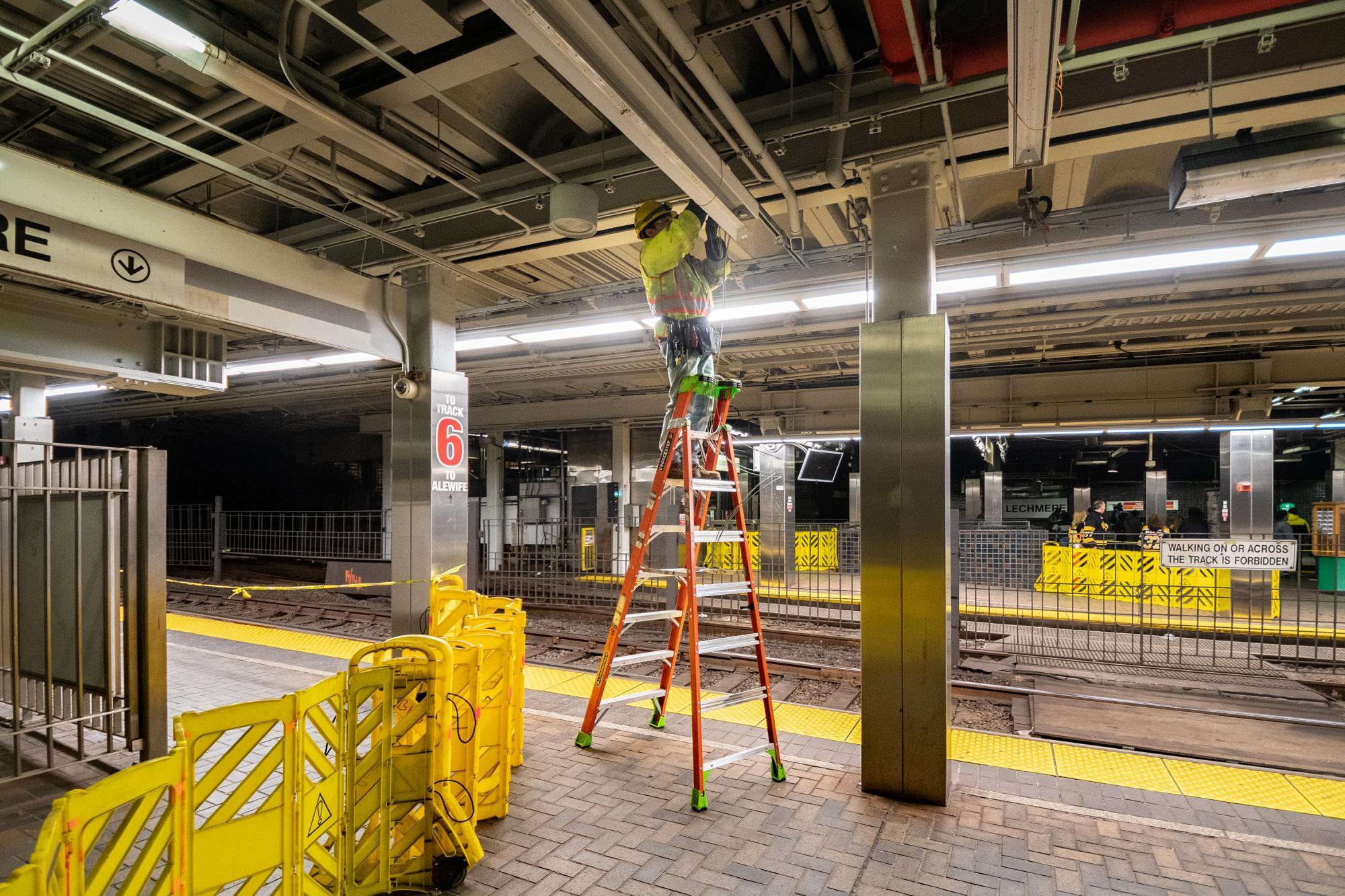 A crewman on a ladder installs new lights above the Green Line at Park Street