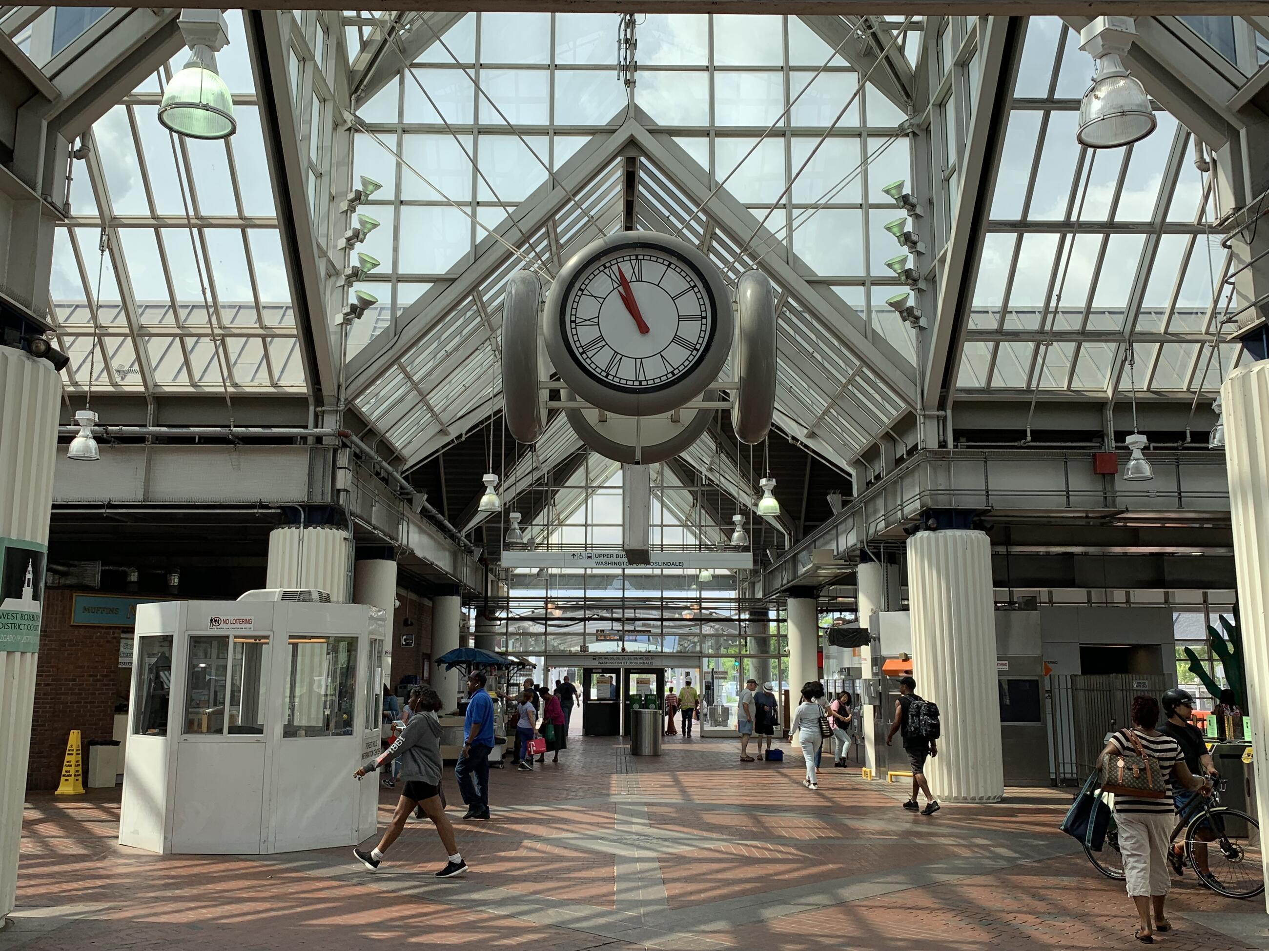 A photo of the interior of Forest Hills station, showing the clock and facing towards the upper busway. Many people are walking through the station.