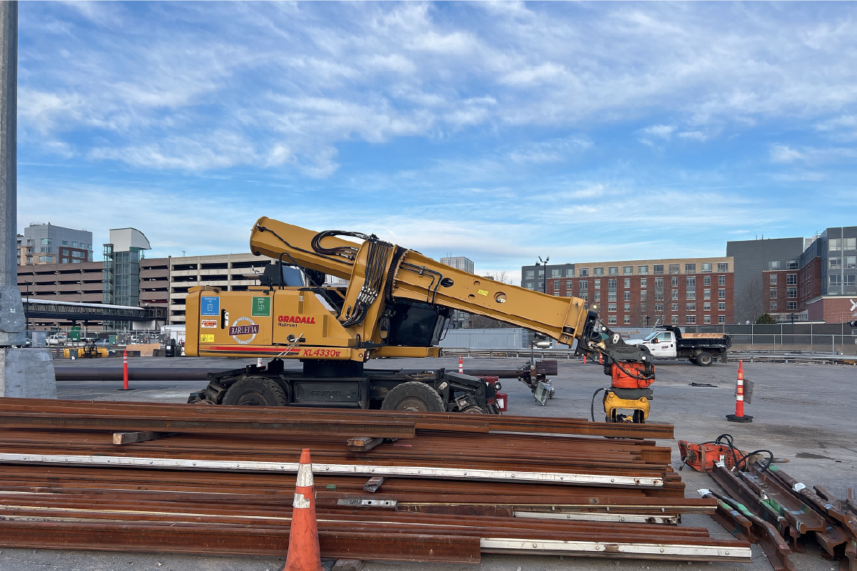 a pile of rail outside next to construction equipment 