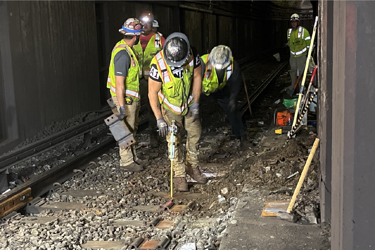 six crew members with hard hats and head lamps on tracks near the opening on a tunnel