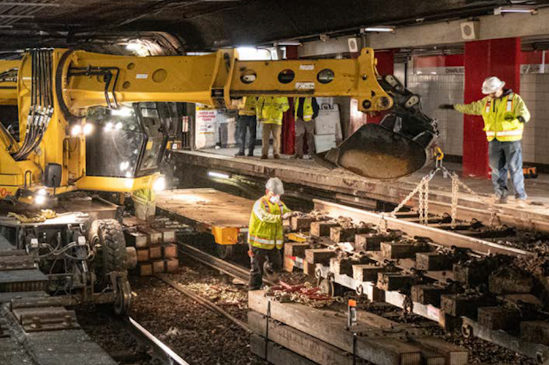 Construction workers use an excavator to move new tracks