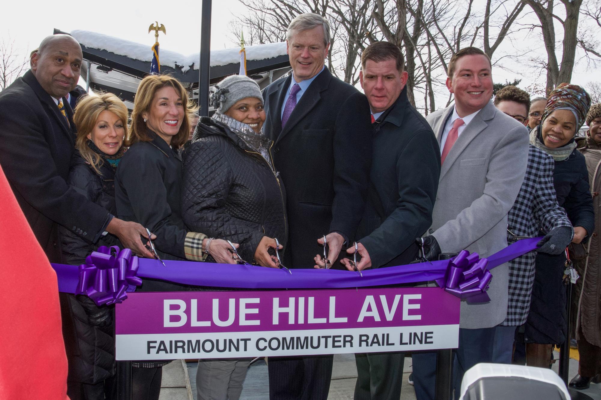 A group of elected officials and community members cut a purple ribbon to celebrate the opening of the Blue Hill Ave station.