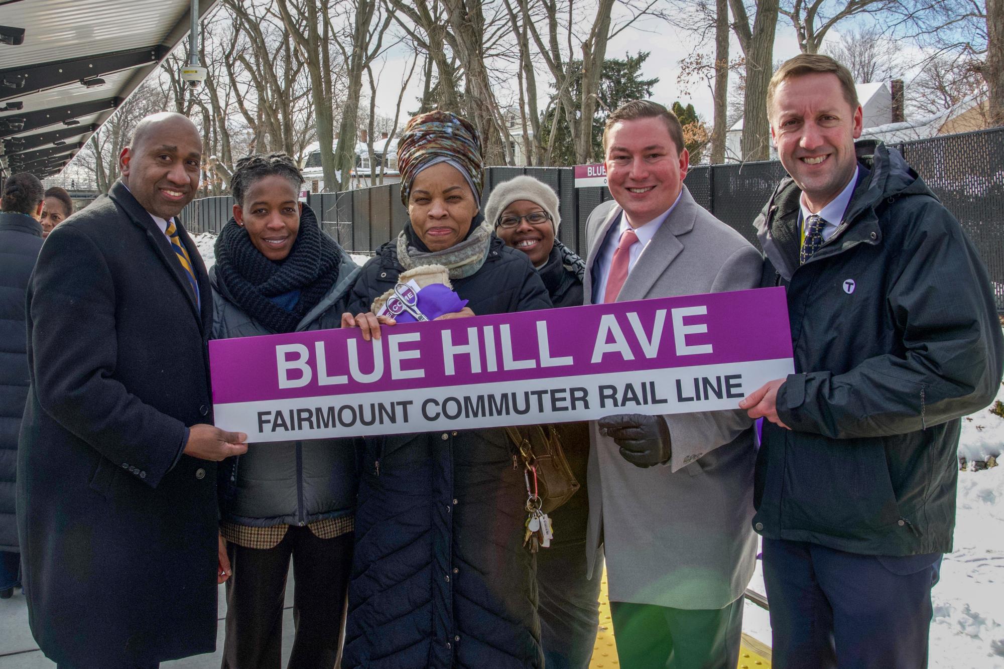 A group of communitiy advocates and MBTA General Manager Steve Poftak pose on the platform with a new station sign.