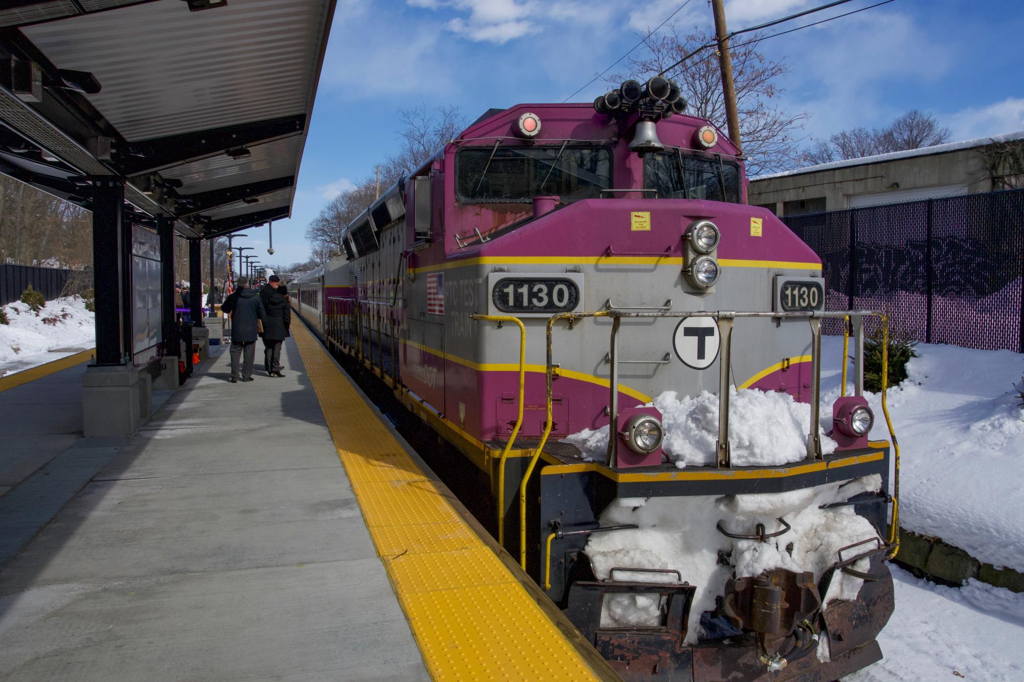 A Commuter Rail train with snow pulls up to the new station's platform.