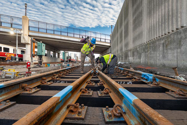 Two personnel in personal protective equipment (PPE) perform rail work at Cabot Yard