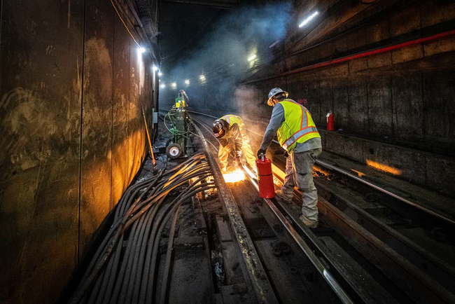 Two personnel perform rail work at Harvard Station